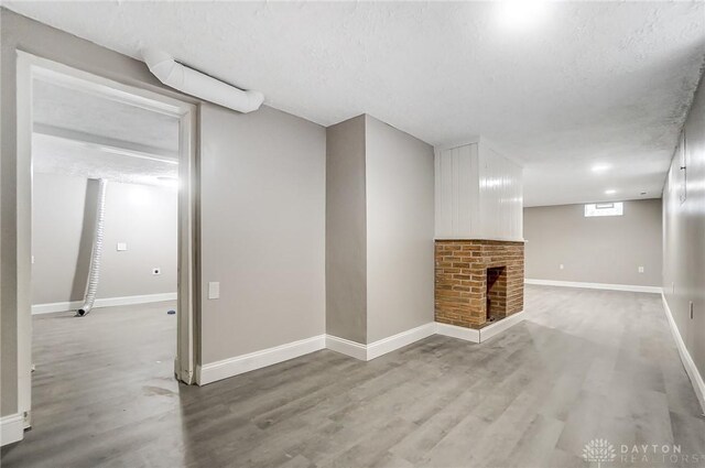 unfurnished living room with hardwood / wood-style flooring, a textured ceiling, and a brick fireplace