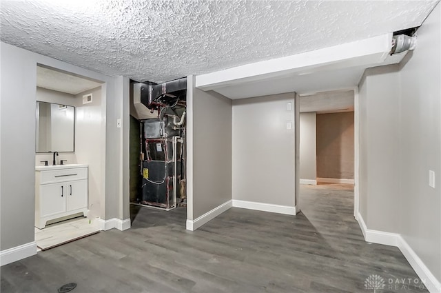 hallway with a textured ceiling, hardwood / wood-style flooring, heating unit, and sink