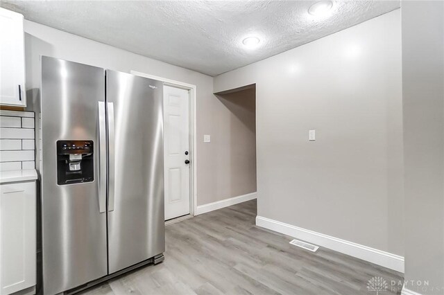 kitchen with stainless steel fridge with ice dispenser, a textured ceiling, decorative backsplash, white cabinets, and light wood-type flooring