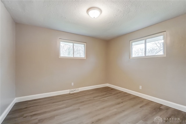 spare room featuring a textured ceiling, hardwood / wood-style flooring, and a healthy amount of sunlight