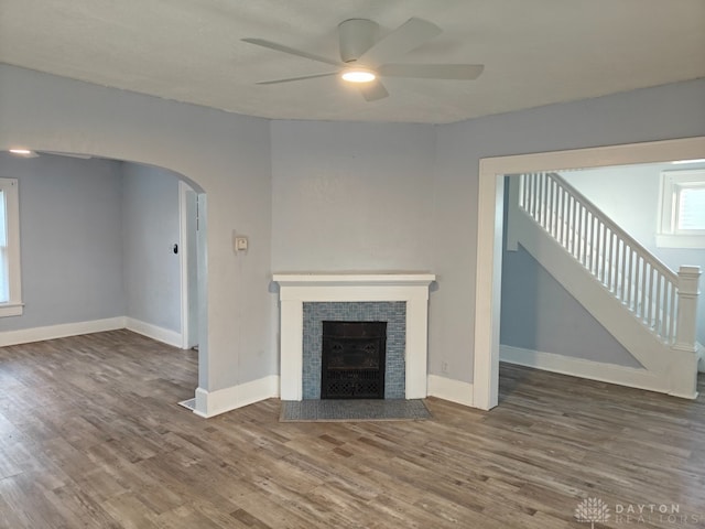 unfurnished living room featuring hardwood / wood-style flooring, ceiling fan, and a tiled fireplace