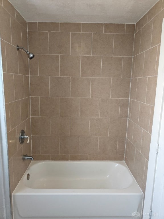 bathroom with a textured ceiling and tiled shower / bath