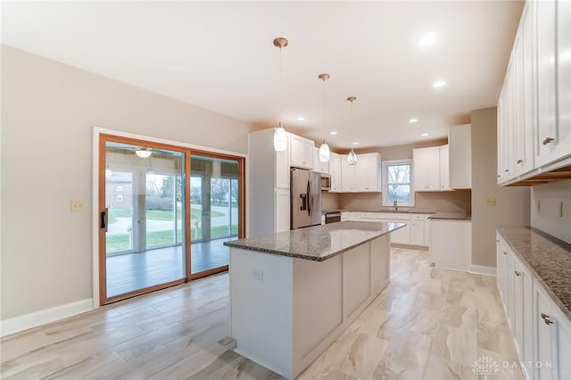 kitchen featuring a center island, decorative light fixtures, stone countertops, white cabinetry, and stainless steel appliances