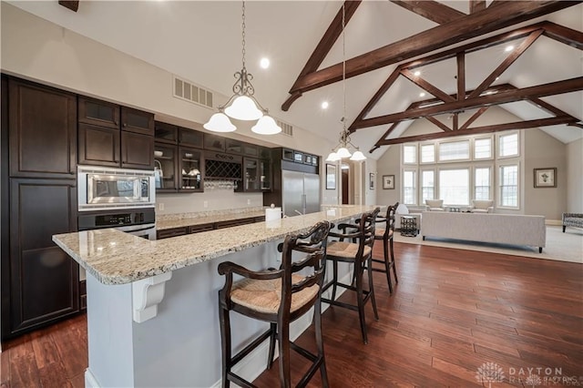 kitchen featuring built in appliances, dark wood-type flooring, high vaulted ceiling, and a large island