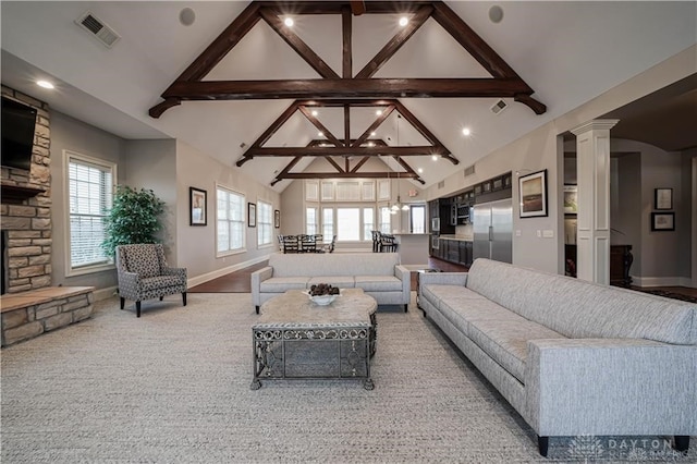 carpeted living room featuring beam ceiling, decorative columns, high vaulted ceiling, and a stone fireplace