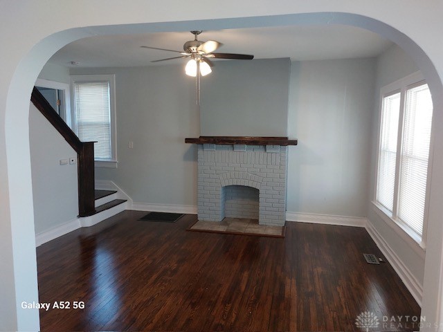 unfurnished living room featuring ceiling fan, a fireplace, and dark wood-type flooring