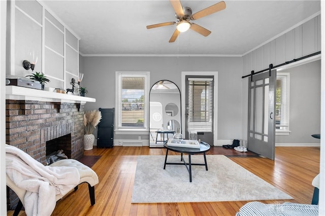 living area with a ceiling fan, a fireplace, hardwood / wood-style flooring, crown molding, and a barn door