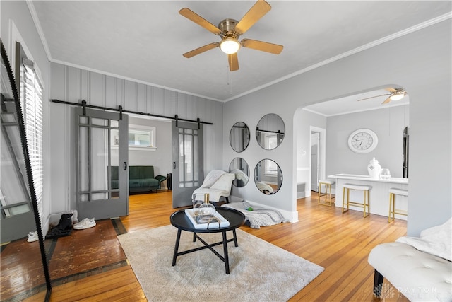 living room featuring a barn door, hardwood / wood-style flooring, ceiling fan, and ornamental molding