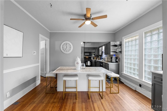 kitchen featuring light hardwood / wood-style flooring, a breakfast bar area, a kitchen island, black appliances, and ornamental molding