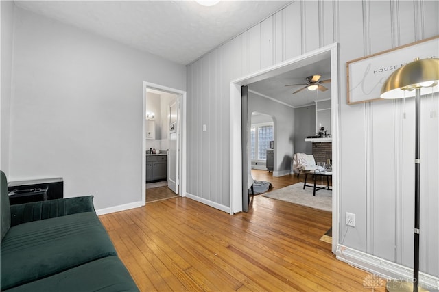 living room with a brick fireplace, ceiling fan, hardwood / wood-style floors, and ornamental molding