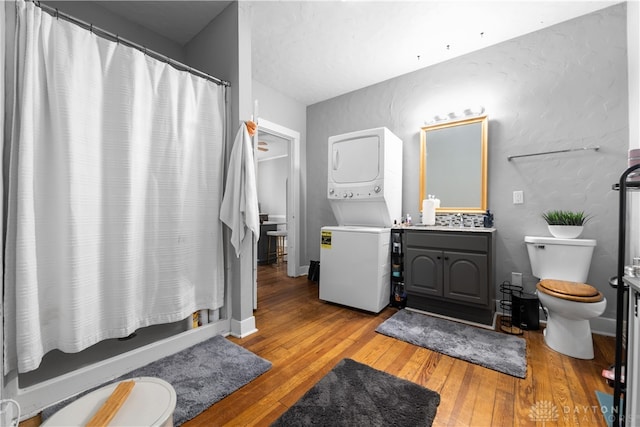 full bathroom featuring hardwood / wood-style floors, vanity, toilet, and stacked washer and clothes dryer