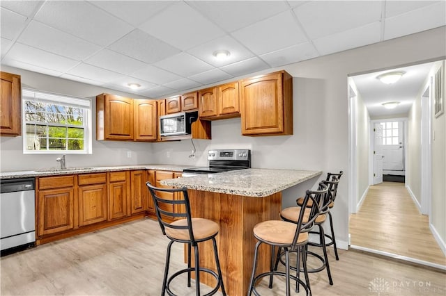 kitchen with sink, stainless steel appliances, a wealth of natural light, light stone countertops, and a kitchen bar