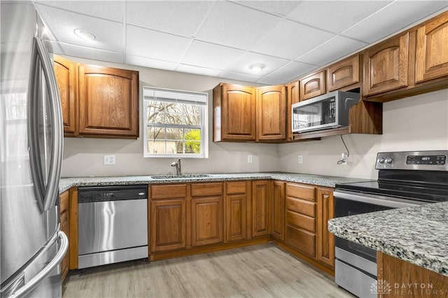 kitchen featuring light stone counters, appliances with stainless steel finishes, light hardwood / wood-style floors, and sink