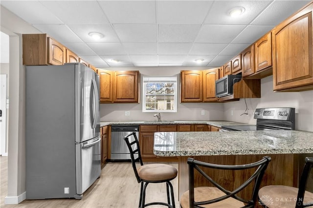 kitchen featuring sink, a kitchen breakfast bar, kitchen peninsula, stainless steel appliances, and light stone countertops