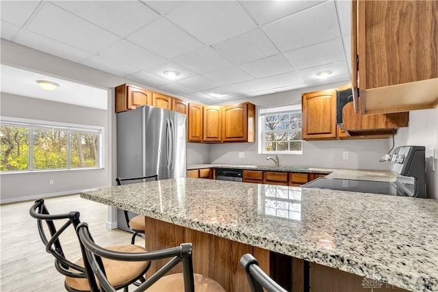 kitchen featuring a breakfast bar, a paneled ceiling, light stone counters, kitchen peninsula, and stainless steel appliances