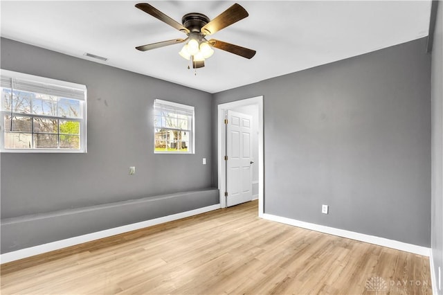 empty room with plenty of natural light, ceiling fan, and light wood-type flooring