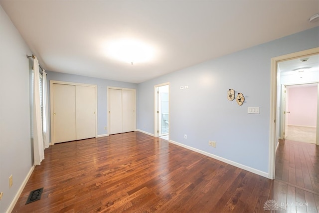 unfurnished bedroom featuring ensuite bathroom, dark hardwood / wood-style flooring, and two closets