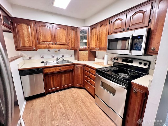 kitchen with light wood-type flooring, appliances with stainless steel finishes, backsplash, and sink