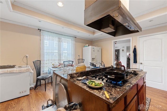 kitchen featuring stainless steel gas cooktop, white refrigerator with ice dispenser, range hood, light hardwood / wood-style floors, and ornamental molding