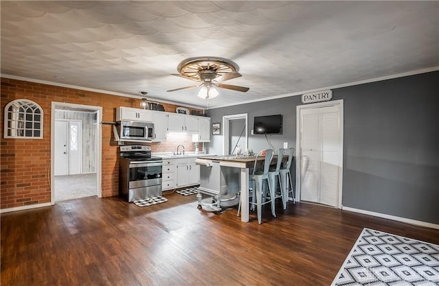 kitchen with appliances with stainless steel finishes, dark hardwood / wood-style floors, white cabinets, a kitchen bar, and crown molding