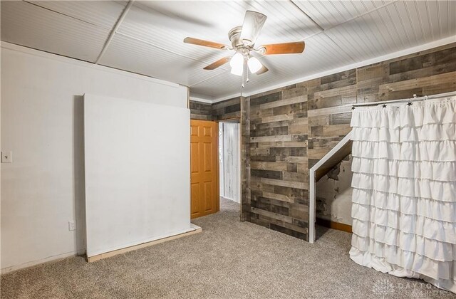 basement with carpet floors, ceiling fan, and wooden walls