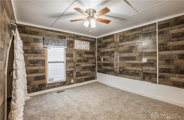 empty room with carpet flooring, wooden walls, and ceiling fan