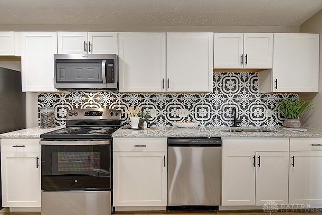 kitchen featuring light stone countertops, decorative backsplash, stainless steel appliances, sink, and white cabinetry