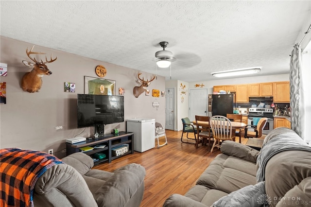 living room with a textured ceiling, light wood-type flooring, and ceiling fan