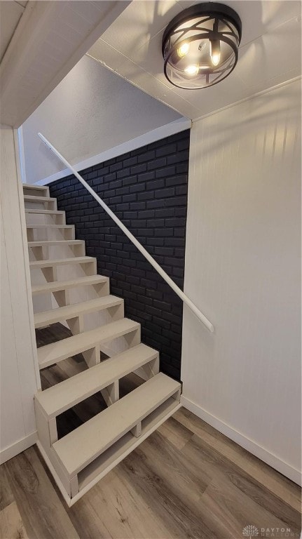 stairway featuring wood-type flooring and brick wall