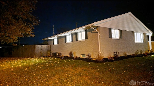 property exterior at night featuring a lawn and central AC