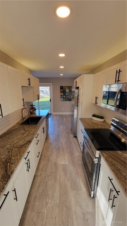 kitchen featuring sink, stainless steel appliances, dark stone counters, white cabinets, and light wood-type flooring