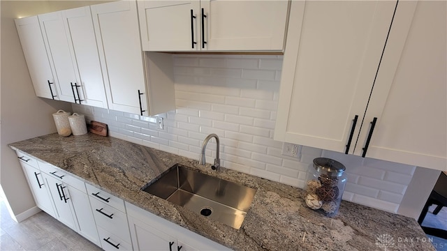 kitchen featuring stone countertops, white cabinetry, sink, and tasteful backsplash