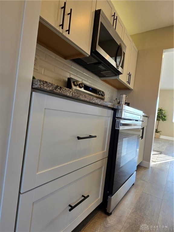 kitchen featuring white cabinets, tasteful backsplash, stainless steel appliances, and dark stone counters