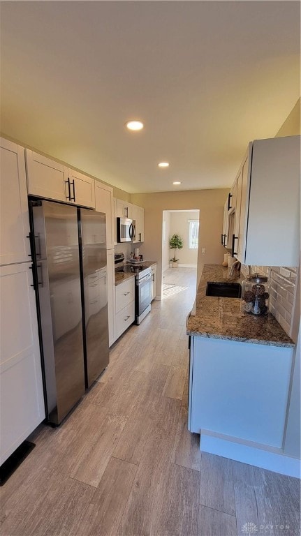 kitchen with sink, stainless steel appliances, dark stone counters, light hardwood / wood-style floors, and white cabinets