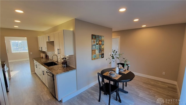 kitchen featuring dishwasher, dark stone counters, white cabinets, sink, and light hardwood / wood-style floors