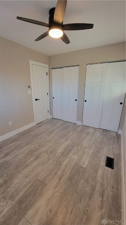 unfurnished bedroom featuring ceiling fan, light hardwood / wood-style floors, and two closets