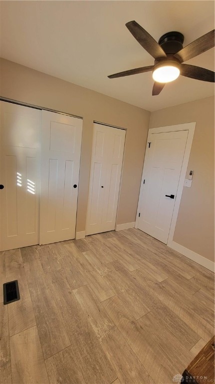 unfurnished bedroom featuring ceiling fan, light hardwood / wood-style flooring, and two closets