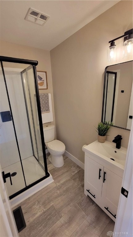 bathroom with vanity, toilet, wood-type flooring, and a shower with door