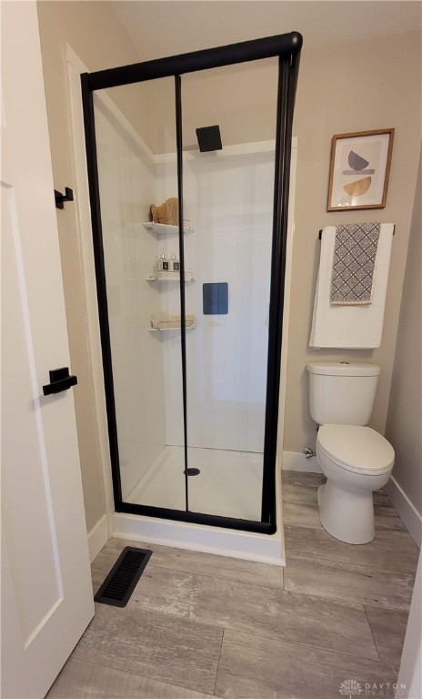 bathroom with wood-type flooring, a shower with shower door, and toilet