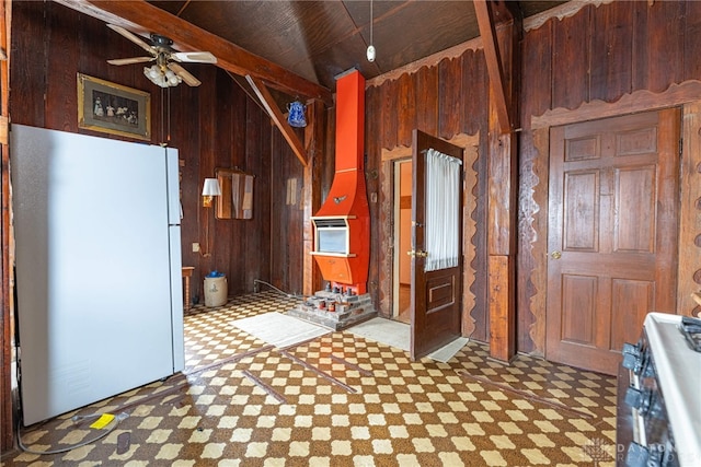 kitchen featuring ceiling fan, lofted ceiling with beams, stainless steel range oven, wood walls, and white fridge