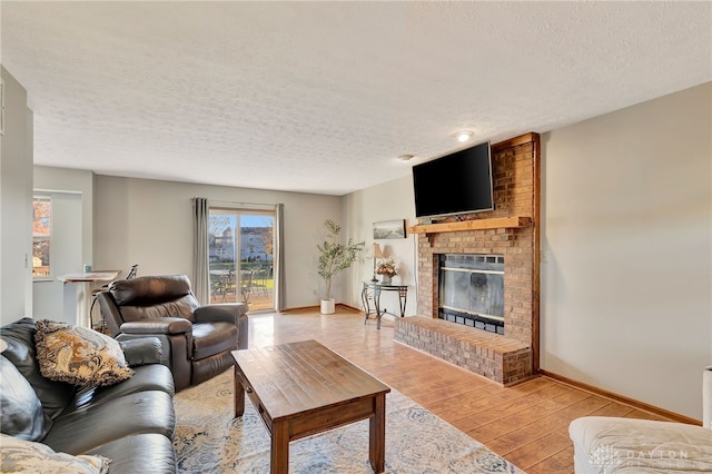 living room with a brick fireplace, a textured ceiling, and light hardwood / wood-style flooring