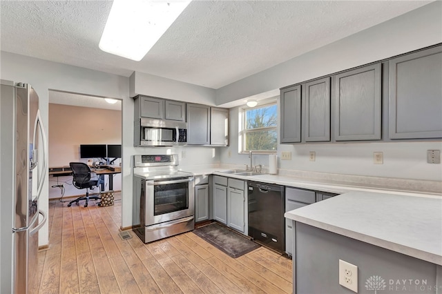 kitchen featuring gray cabinetry, light wood-type flooring, sink, and appliances with stainless steel finishes