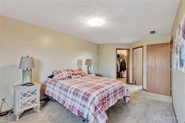 carpeted bedroom featuring a textured ceiling, a walk in closet, and a closet