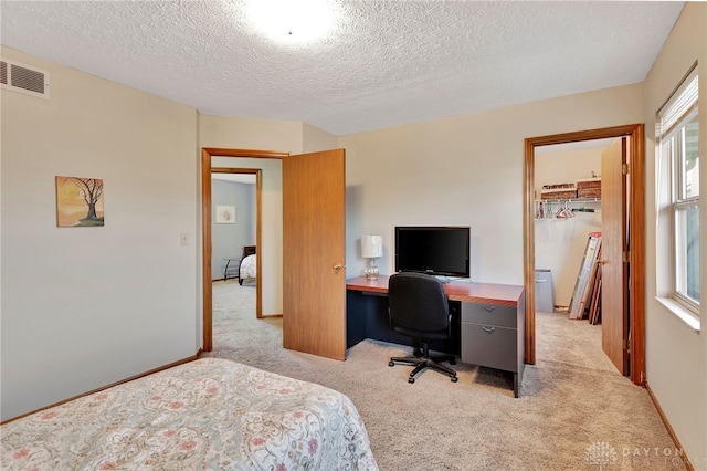 bedroom featuring a textured ceiling, a walk in closet, light carpet, and a closet