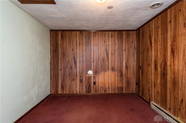 unfurnished room featuring a textured ceiling, wood walls, baseboard heating, and dark colored carpet