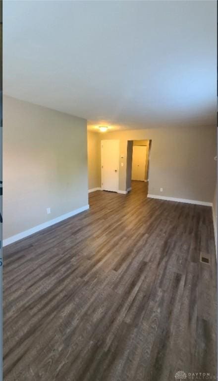 empty room with visible vents, baseboards, and dark wood finished floors