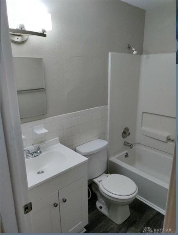 bathroom featuring shower / tub combination, toilet, wood finished floors, vanity, and tile walls