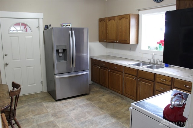 kitchen featuring stainless steel refrigerator with ice dispenser, electric range, tile counters, and sink