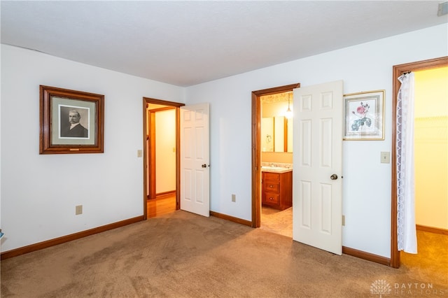 unfurnished bedroom with sink, ensuite bathroom, a walk in closet, light carpet, and a closet