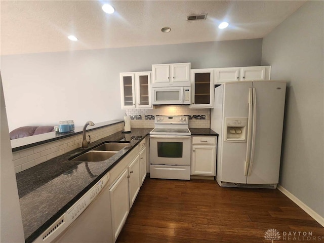 kitchen featuring tasteful backsplash, sink, dark stone countertops, dark wood-type flooring, and white appliances